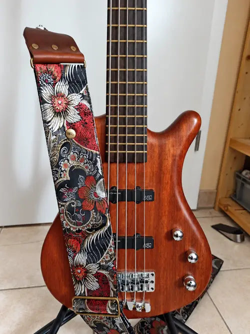 Deluxe-Bassgurt mit rot-weißem Blumenmuster auf Schwarz und braunen Lederlaschen an einem E-Bass in Rotbraun