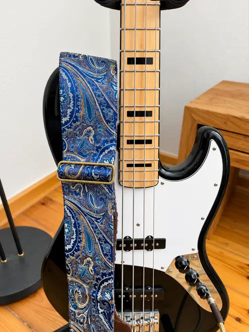 Deluxe-Bassgurt mit blauem Paisley-Muster und goldenen Akzenten an einem schwarzen E-Bass mit weißem Schlagbrett