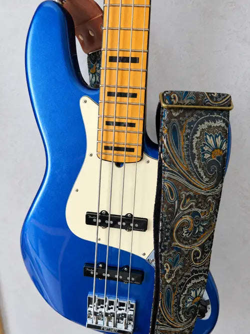 Schwarzer Bassgurt mit Paisley-Muster und braunen Lederlaschen an einem blau metallic lackierten E-Bass