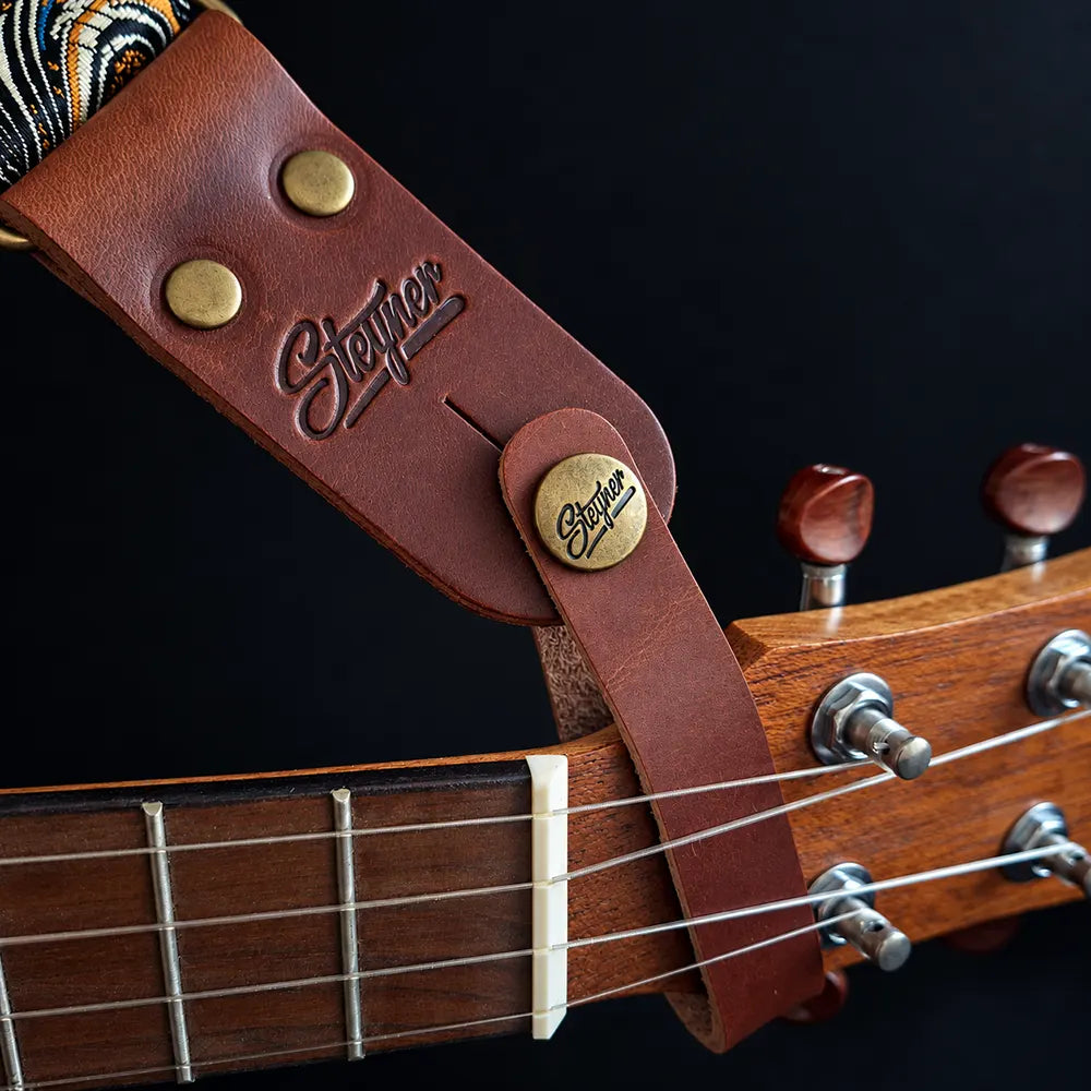 Gurtverbinder (Strapbutton) für Ukulele und Mandoline aus rotbraunem Echtleder mit Alt-Messing-Schraube, hier mit einem Ukulelengurt aus Brokatstoff an einer Ukulele