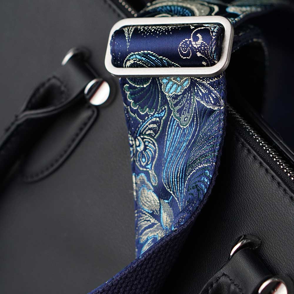 Breiter Schulteriemen in blau mit Muster und edlem Glanz auf einer schwarzen Leder Handtasche
