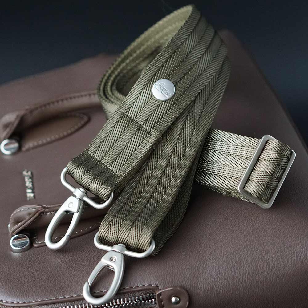 Luxus Designer Schulterriemen in grün khaki und silbernen Karabinerhaken auf einer braunen Handtasche aus Leder