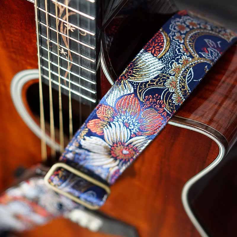Blauer Gitarrengurt mit Glanz und Blumen Muster auf einer Akustik Gitarre