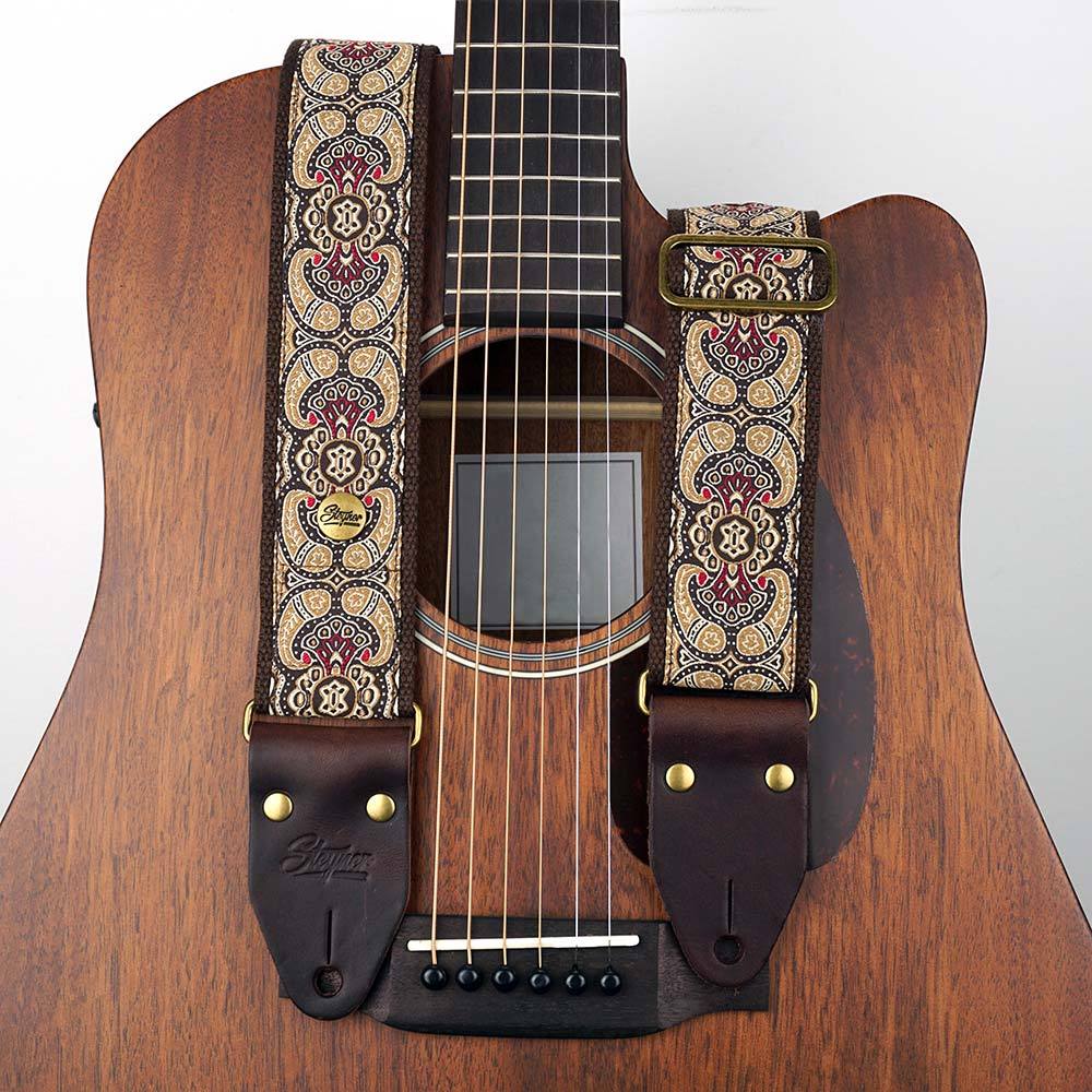 Brauner Gitarrengurt in Retro Optik und buntem Paisley Muster liegt auf einer Akustikgitarre