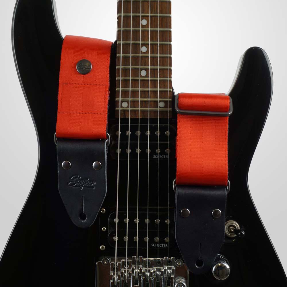 Hochwertiger Gitarrengurt rot aus Sicherheitsgurtband auf einer schwarzen Gitarre