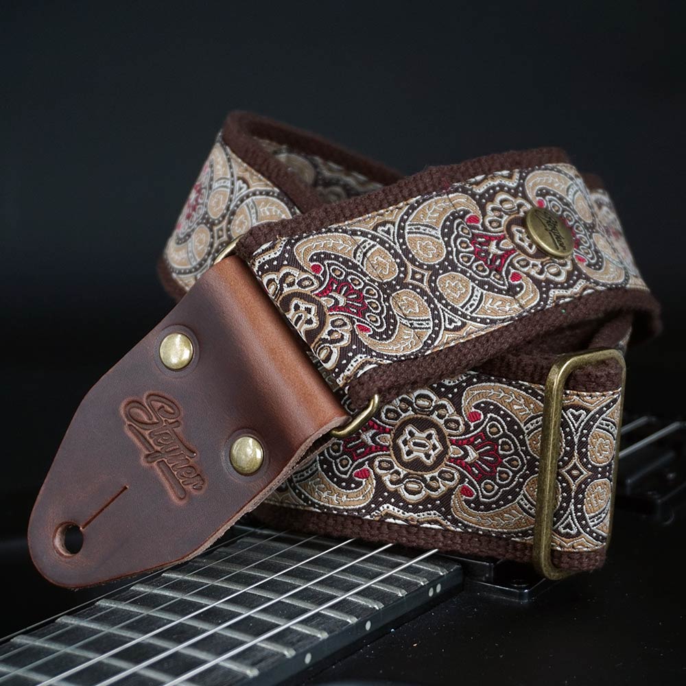 Brauner Gitarrengurt in Retro Optik und buntem Paisley Muster liegt auf einer E Gitarre