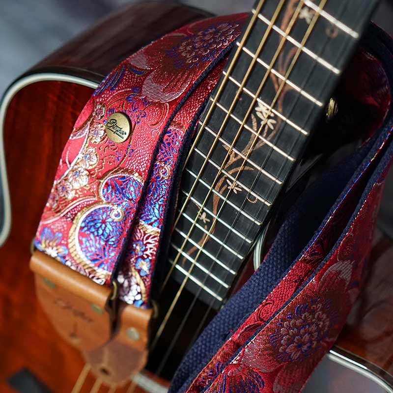 edleer Gitarrengurt in rot glänzend mit Blumen Muster auf einer braunen Akustikgitarre von Taylor